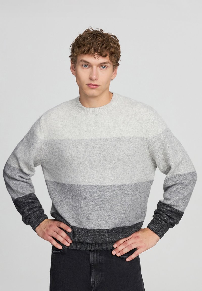 Maglioncino a righe grigio e bianco, con colletto rotondo, polsini e orlo a costine. Presenta una sfumatura dal grigio chiaro al grigio scuro.