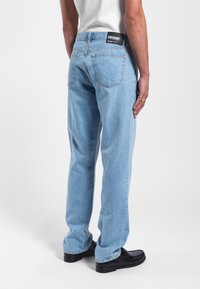 Jeans in denim blu chiaro con design a gamba dritta, caratterizzati da tasche posteriori e un'etichetta nera del marchio sulla vita. Rifiniti con cuciture visibili.