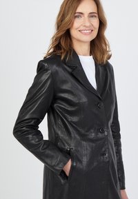 Schwarzer Ledermantel mit maßgeschneidertem Design, eingeschnittenen Revers, Knopfverschluss und Seitentaschen. Glatte Textur und figurbetonte Silhouette.