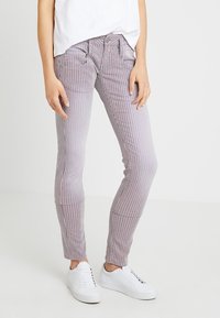 Randiga byxor i röd och vit tyg, slim fit med sidofickor och en synlig dragsko. Bärs med vita sneakers och en lös vit topp.