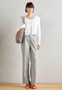 White long-sleeve cropped cardigan over a white shirt, paired with light gray pinstriped trousers and red knotted sandals. Gray tote bag.