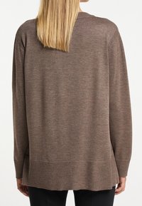 Brązowy sweter dzianinowy o luźnym kroju, z prążkowanymi mankietami i dołem oraz miękką fakturą. Charakteryzuje się nieco dłuższym tyłem dla dodatkowego zakrycia.