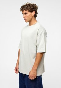 T-shirt oversize gris clair à manches courtes, col rond et texture douce, associé à un jean en denim foncé ample.