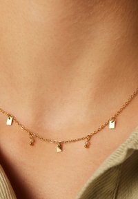 Collier en chaîne en or avec de petits pendentifs rectangulaires et des accents ronds, conçu avec un motif de maillon délicat et une texture lisse.