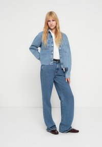 Denimjakke og vide jeans i lyseblå. Jakken har et kort snitt og frontlommer. Jevn tekstur med minimal slitasje.