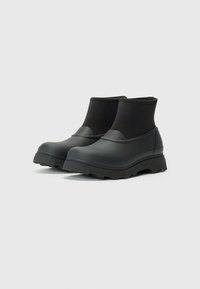 Bottes de cheville noires imperméables avec un extérieur en caoutchouc lisse et une semelle texturée, dotées d'une tige de cheville ajustée pour un maintien sécurisé.