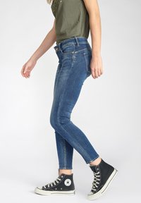 Jeans skinny en denim de couleur bleue avec une taille mi-haute et un léger délavage. Associés à des baskets montantes noires avec des accents blancs.