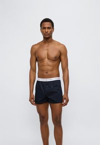 Ανδρικά εσώρουχα boxer σε ναυτικό μπλε χρώμα με λευκή ελαστική ζώνη μέσης, με ετικέτα "TOMMY HILFIGER". Διαθέτουν μπροστινό κουμπί και κλασική γραμμή. Ομαλή υφή υφάσματος.