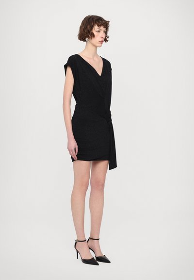 Robe noire, courte, scintillante avec un décolleté en V, des manches courtes et un détail torsadé sur le côté. Portée avec des talons à bride de cheville noirs. Design simple et ajusté.