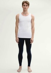 White sleeveless tank top paired with form-fitting navy leggings, made of smooth fabric, presented on a standing male figure.
