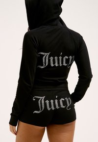 Schwarzes Hoodie- und Shorts-Set mit "Juicy" aus Strass auf der Rückseite. Das Material wirkt weich mit einer glatten Textur. Mit Kapuze.