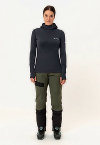 Dunkelgraues Langarmoberteil mit strukturiertem Design, kombiniert mit olivgrünen Hosen, schwarzen Akzenten und Skistiefeln mit blauen Details.