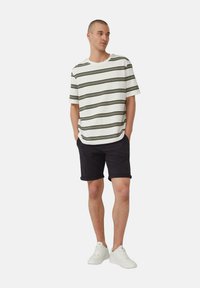 Gestreept katoenen t-shirt met ronde hals, gecombineerd met donkere opgerolde shorts en witte sneakers. Bevat horizontale olijf- en zwarte strepen.