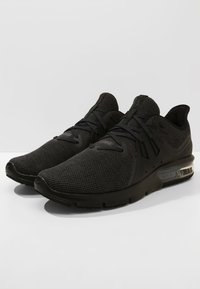 Czarne buty sportowe z siateczkową cholewką, teksturowaną powierzchnią, minimalistycznym wzornictwem oraz widoczną jednostką poduszkową w podeszwie.