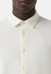 Witte polo met een klassieke kraag, voorzien van een knoopsluiting met licht contrasterende knopen en een zachte, gestructureerde stof.