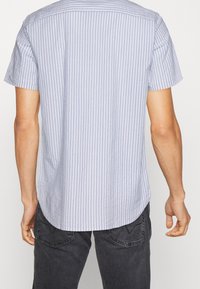 Camisa de manga corta con cuello, de rayas verticales en azul claro y blanco, confeccionada en un tejido texturizado, con dobladillo curvado y corte estándar.