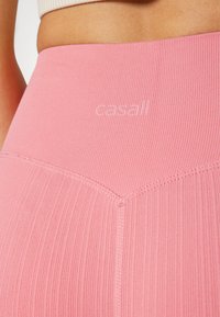 Leggings sportive a coste di un delicato rosa, caratterizzati da una texture liscia, una vita alta e un marchio sottile ricamato vicino alla parte superiore.