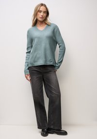 Helles blauer, gerippter Strickpullover mit V-Ausschnitt und diagonalen Mustern, kombiniert mit lockeren schwarzen Jeans und schwarzen Ankle Boots.
