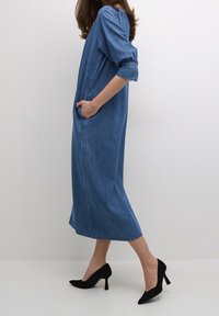 Denim-mekko, jossa on löysä istuvuus, kolmiviidennys hihat, sivutaskut ja polvimittainen helma. Yhdistetty mustiin korkokenkiin.