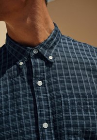Marineblauwe geruite overhemd met een button-down kraag, voorzien van witte knopen, een borstzak en textiel met verticale en horizontale lijnen.