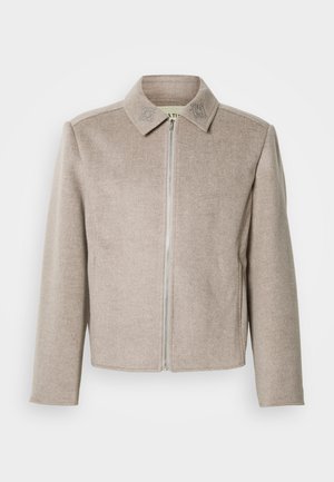 Svetlobéžová bunda na zips s golierom, vyrobená z hladkej, textúrovanej tkaniny s jemnými vyšívanými detailmi na golieri.