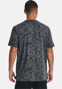 Grå atletisk t-shirt med ett svart sprickmönster, korta ärmar, mjukt tyg och rund halsringning. Bakifrån med logotyp vid nacken.