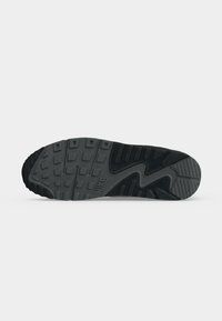 Σόλα μαύρου παπουτσιού Nike με υφή πέλματος που διαθέτει μοτίβο τετράγωνων και ζιγκζάγκ σχημάτων σε απλό ανοιχτό γκρι φόντο.