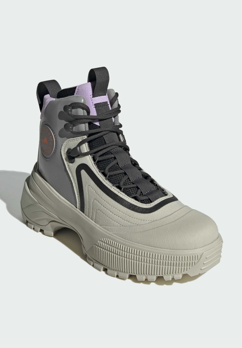 Wysokie buty sportowe w odcieniu szarym i delikatnym purpurowym, z teksturowaną gumową podeszwą, skomplikowanym sznurowaniem oraz okrągłym logo po boku.