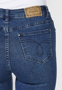 Gros plan de la poche arrière d'un jean en denim bleu foncé avec un motif cousu et une étiquette en cuir marron portant l'inscription "Koroshi Denim Collection."