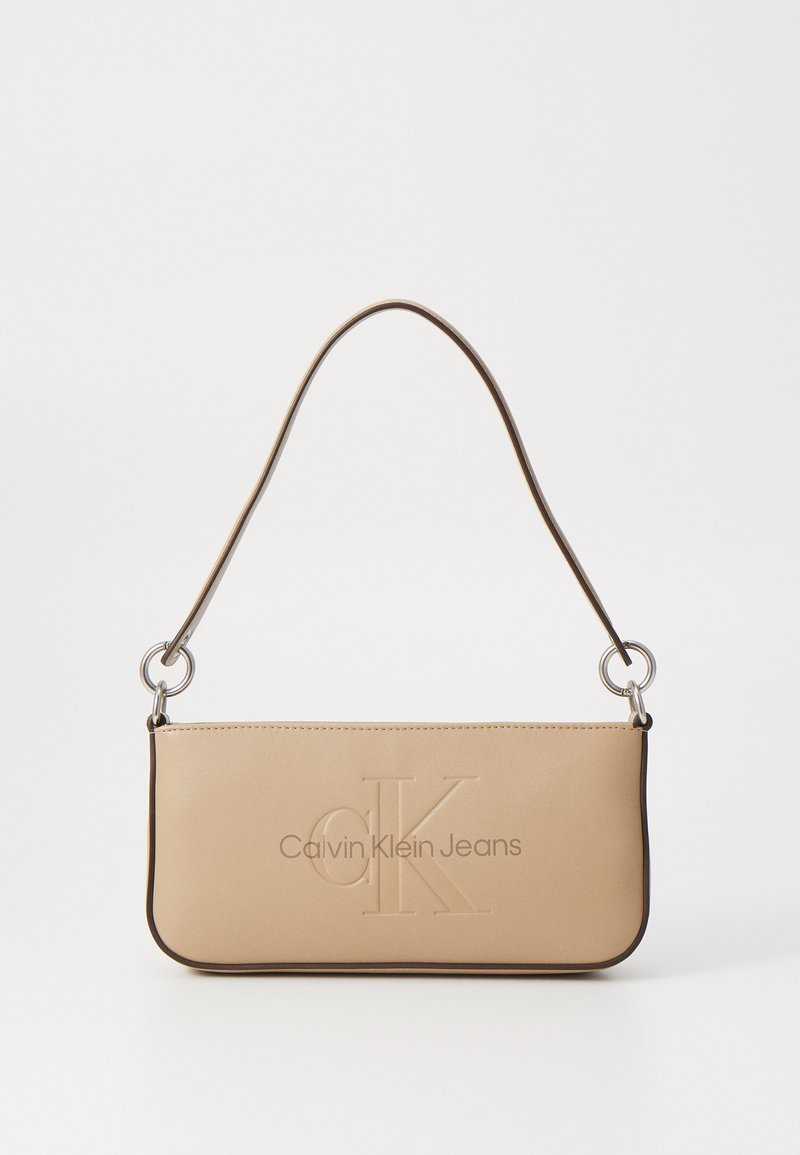Beige kunstlæder håndtaske med præget "CK" logo, sølvhardware og en tynd skulderrem. Glat tekstur og minimalistisk design.