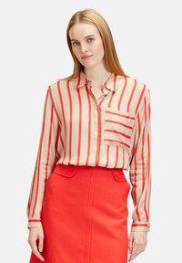 Beige blouse with red vertical stripes, long sleeves, collar, and chest pocket, paired with a bright red skirt. Smooth texture.