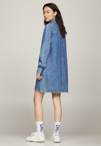 Vestido camisa de mezclilla en azul claro, con mangas largas, cierre de botones en la parte delantera y un corte relax. Combinado con zapatillas blancas y calcetines de estampado.