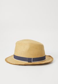 Sombrero de paja con ala ancha, de color tostado y tejido texturizado. Presenta una banda de tela azul oscuro con ribete blanco en la base. Los bordes están deshilachados.