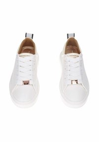 Baskets blanches avec lacets plats, tige en cuir lisse, bout arrondi et détail logo métallique sur le côté. Tirette noire au niveau du talon.