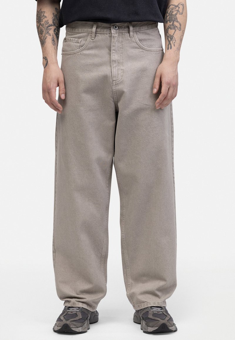 Pantalones de mezclilla beige de corte relajado con cintura alta, bolsillos frontales y una textura suave, combinados con zapatillas grises.