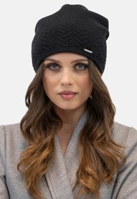 Beanie nera lavorata a maglia con motivo a zigzag, realizzata in materiale morbido. Presenta un piccolo tag argento sul davanti.