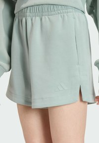 Light green athletic shorts made of soft fabric, featuring an elastic waistband, side slits, and a subtle logo detail near the hem.