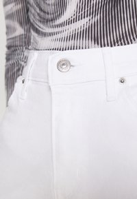 White denim jeans feature a zip fly, metal button closure, and subtle stitching details. A textured black-and-white patterned top is visible above.