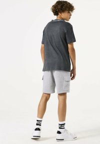 T-shirt grigia in cotone con vestibilità rilassata, abbinata a pantaloni cargo grigi chiari. Gli accessori includono sneakers bianche e calzini neri a fantasia.