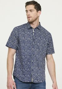 Chemise à manches courtes marine avec motif floral blanc, col boutonné et patte de boutonnage contrastante ; tissu léger avec une coupe décontractée.