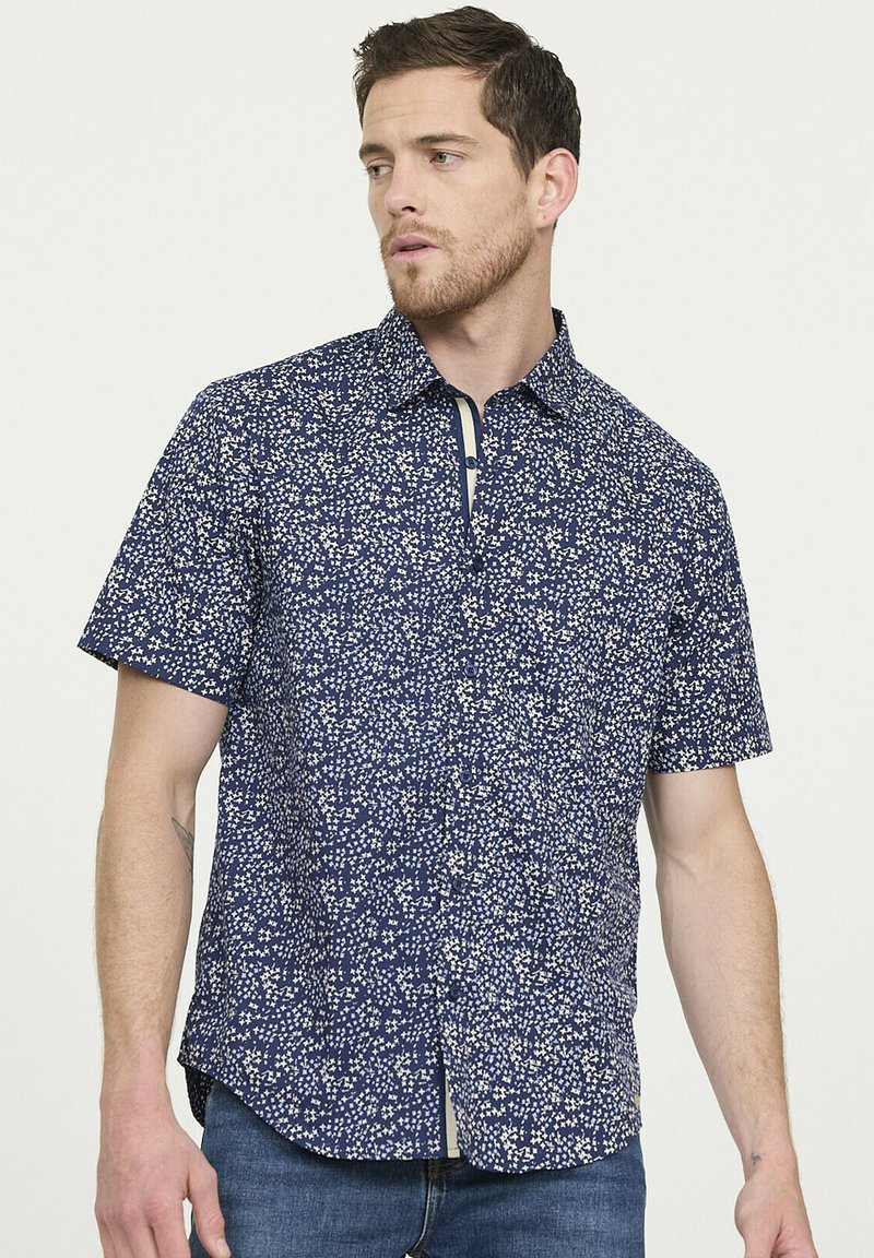 Chemise à manches courtes marine avec motif floral blanc, col boutonné et patte de boutonnage contrastante ; tissu léger avec une coupe décontractée.