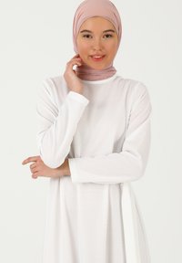 White, long-sleeve dress made of textured fabric, featuring a round neckline and a tie accent. Paired with a light pink hijab.