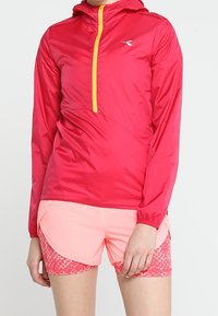 Lightweight, water-resistant red jacket with a yellow zipper and a hood, paired with pink athletic shorts featuring a textured pattern.