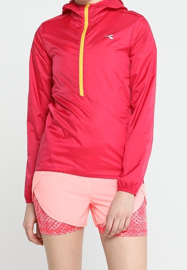 Lightweight, water-resistant red jacket with a yellow zipper and a hood, paired with pink athletic shorts featuring a textured pattern.