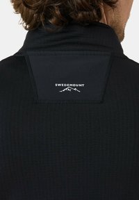 Zwarte sporttop van textiel met een gestructureerde stof, met een hoge kraag, een subtiele logo op de achterkant en contrasterende stiksels.