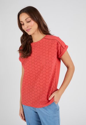 Camiseta roja de manga corta con diseño perforado y pequeños agujeros, cuello redondo, corte relajado y textura suave. Llevada con pantalones azul claro.
