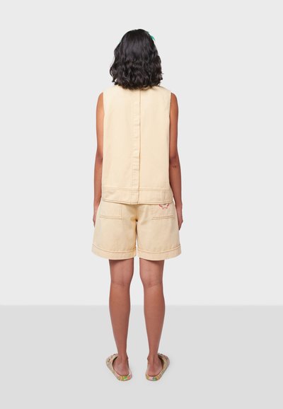 Top senza maniche di un giallo chiaro con dettagli di cucitura e pantaloni shorts abbinati con tasche e ricamo a forma di farfalla sulla schiena.