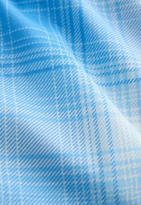 Tissu à carreaux bleu et blanc avec des lignes diagonales et verticales, montrant de doux plis et une texture en vue rapprochée.