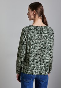 Blusa a maniche lunghe verde e crema con motivo, caratterizzata da un collo rotondo e una vestibilità rilassata. Indossata con jeans in denim blu.