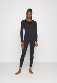 Schwarzes Langarmoberteil und enganliegende Leggings aus Stretchmaterial, mit einem runden Ausschnitt und Logo auf der Brust.